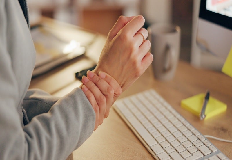 An employee’s wrist hurts during desk work, showcasing Carpal Tunnel Syndrome.