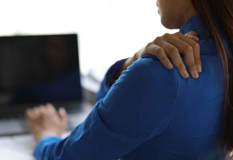 An individual experiencing shoulder injuries while using a laptop, showing discomfort while working
