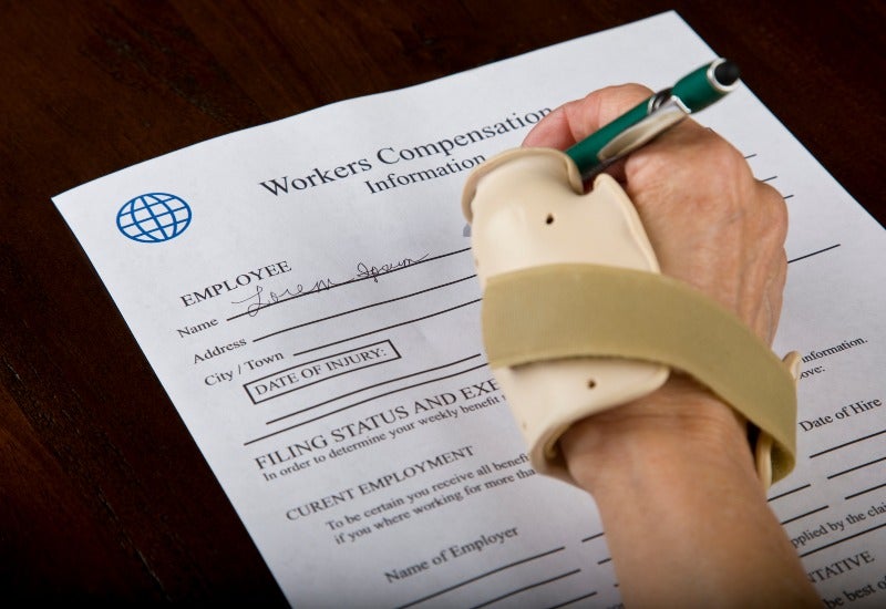 A worker is filling out a workers' compensation claim form with wrist support.