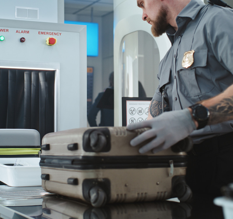TSA worker putting luggage and personal items in trays on conveyor belt
